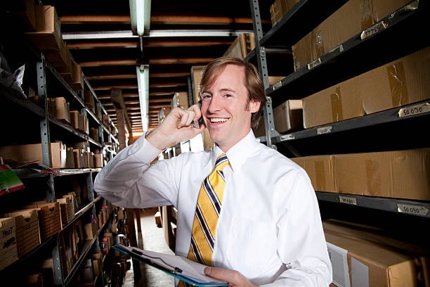 A man talks on a phone in a warehouse environment.